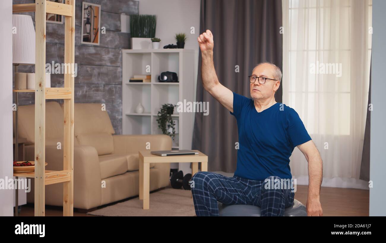 Uomo anziano che fa l'esercitazione di riscaldamento prima dell'addestramento di idoneità. Anziano pensionato sano addestrando sport di salute a casa, esercitandosi attività di idoneità all'età anziana Foto Stock