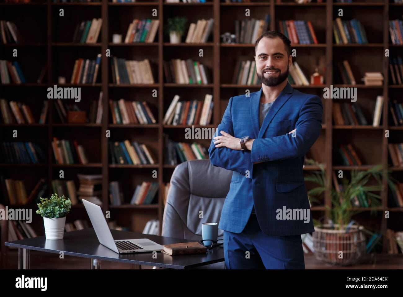 Uomo d'affari giovane in un vestito blu nella biblioteca dell'ufficio. Un uomo si trova sul desktop con un notebook Foto Stock