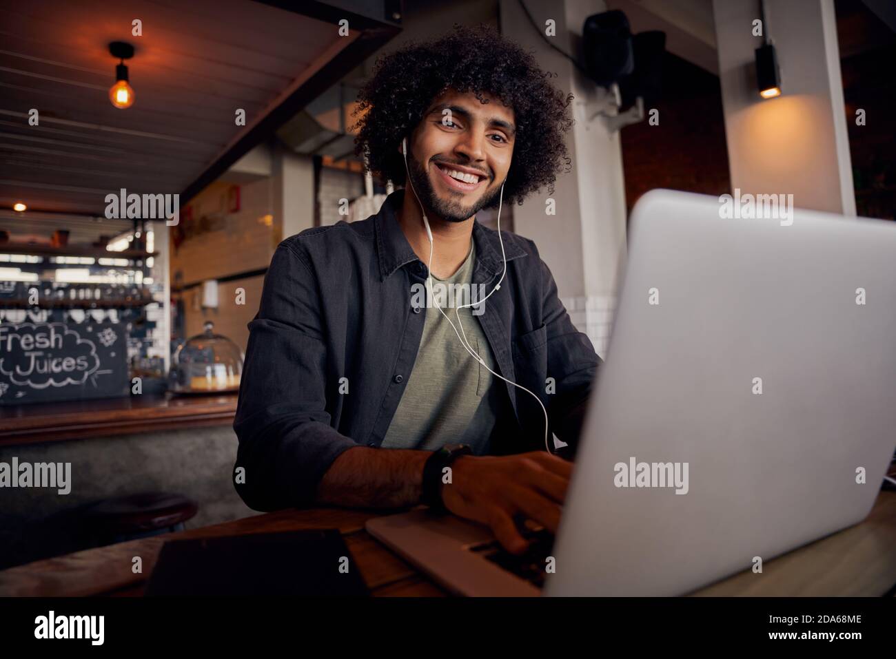 Felice giovane uomo che guarda i video online su computer portatile con auricolari in caffetteria Foto Stock