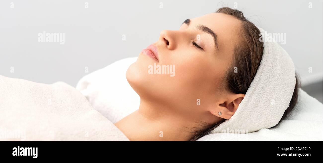 Vista laterale di giovane donna sdraiata su tavolo estetista con occhi chiusi in attesa di una procedura cosmetica in salone di bellezza Foto Stock