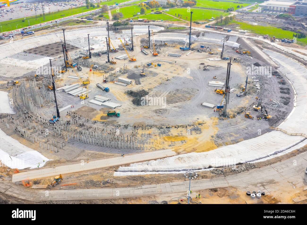 Costruzione di uno stadio, di un complesso espositivo, di un'arena. Le macchine pesanti per la guida di pilastri lavorano nella posa dell'edificio di fondazione. Altezza di visione aerea Foto Stock