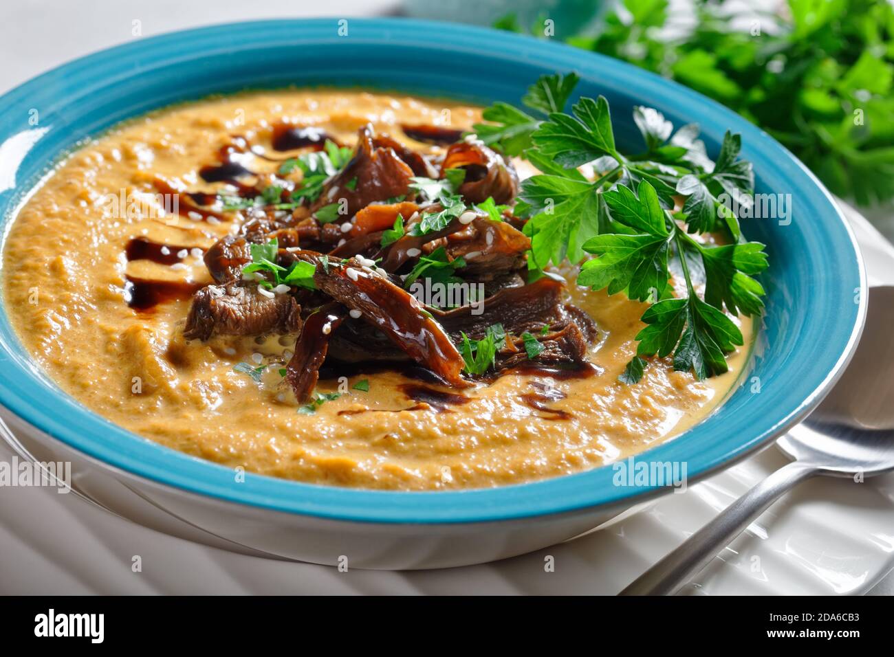 Zuppa di zucca cremosa con brodo di funghi selvatici e latte di cocco condito con semi di sesamo e prezzemolo fresco servito su un ciotola blu con salsa di soia su un li Foto Stock