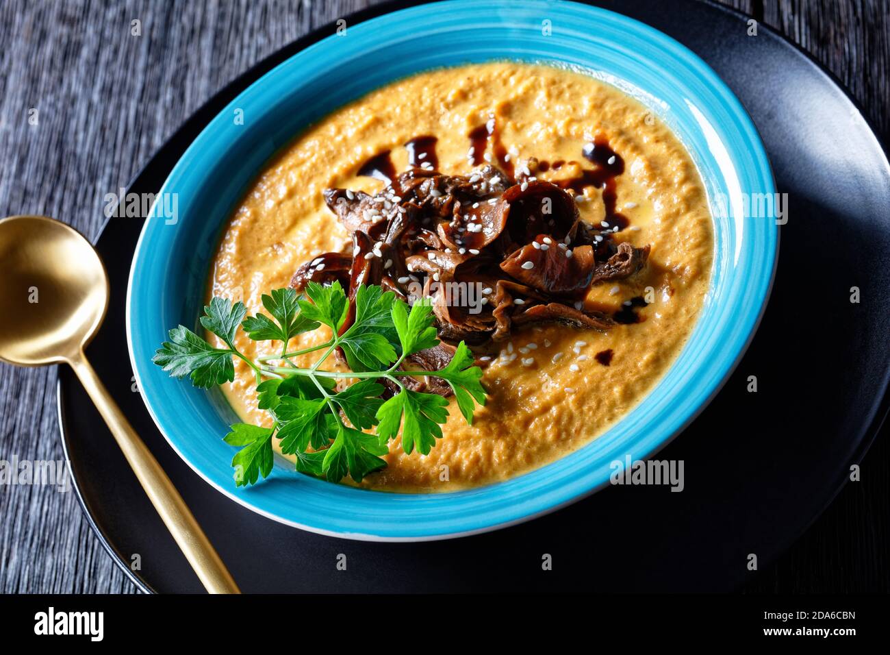 Zuppa di zucca di purea di zucca arrostita e brodo di funghi selvatici, condita con semi di sesamo, piatto vegano comfort, servita su un piatto blu con cucchiaio e ga Foto Stock