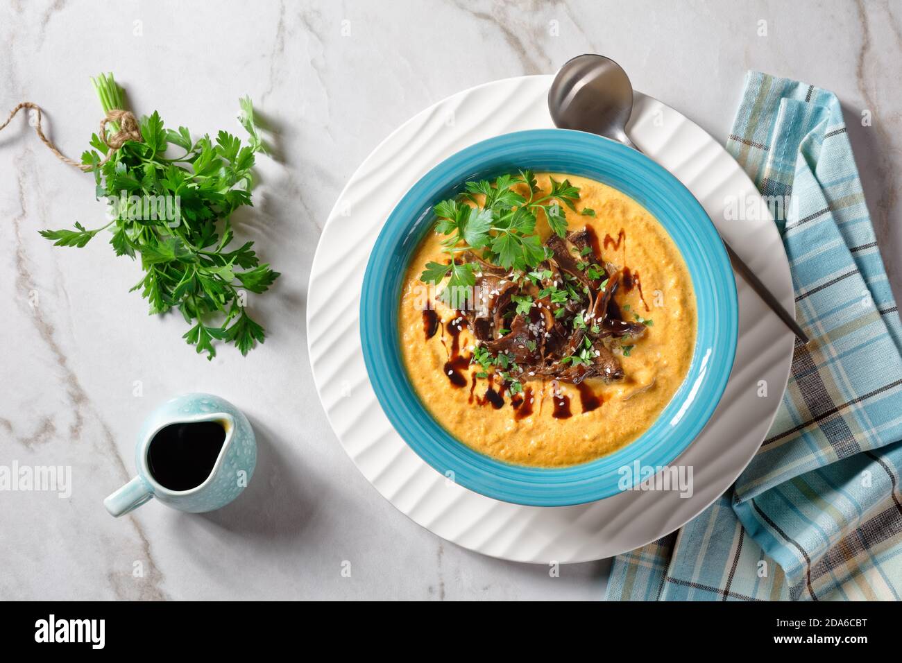 Zuppa di zucca cremosa con brodo di funghi selvatici e latte di cocco condito con semi di sesamo e prezzemolo fresco servito su un ciotola blu con salsa di soia su un li Foto Stock