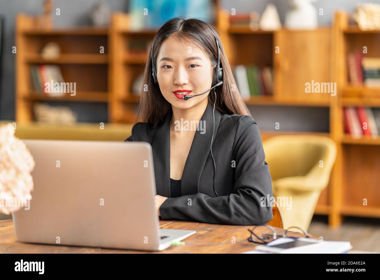 Sorridente rappresentante del servizio di assistenza cinese che consulta il cliente. Ritratto femminile guardando la fotocamera Foto Stock