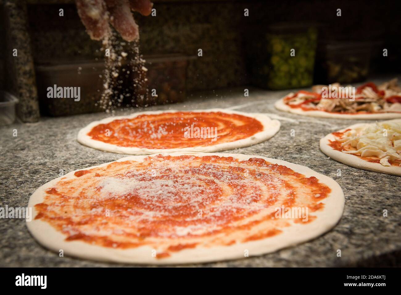 Il pizzaiolo prepara una pizza italiana mettendo il Parmigiano sulla salsa di pomodoro Foto Stock