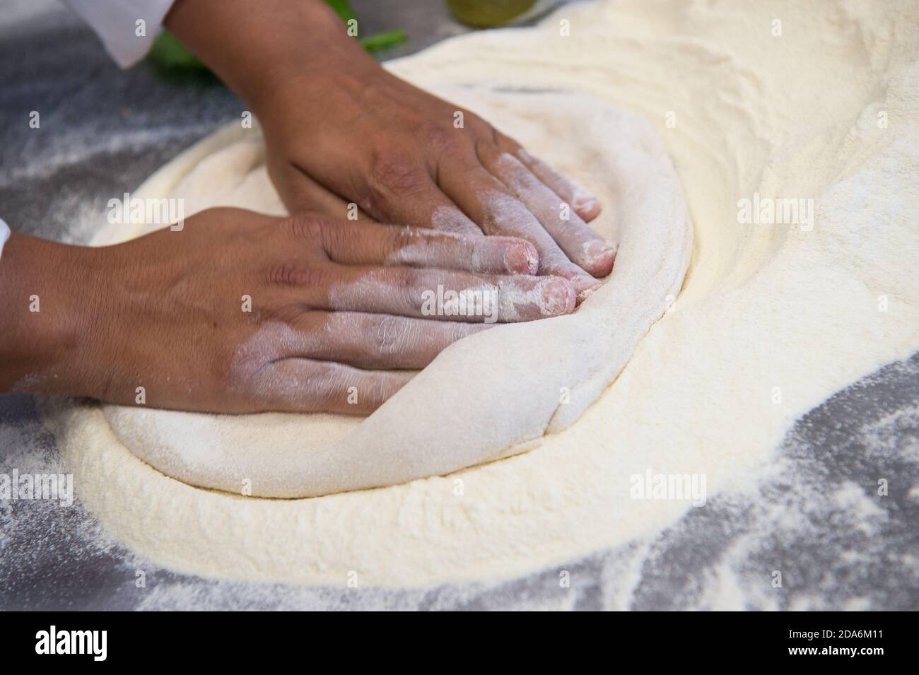 Dettaglio delle mani di uno chef pizzeria che lavora per le varie fasi di preparazione di una vera pizza italiana fatta in casa con farina di lievito e acqua. Foto Stock