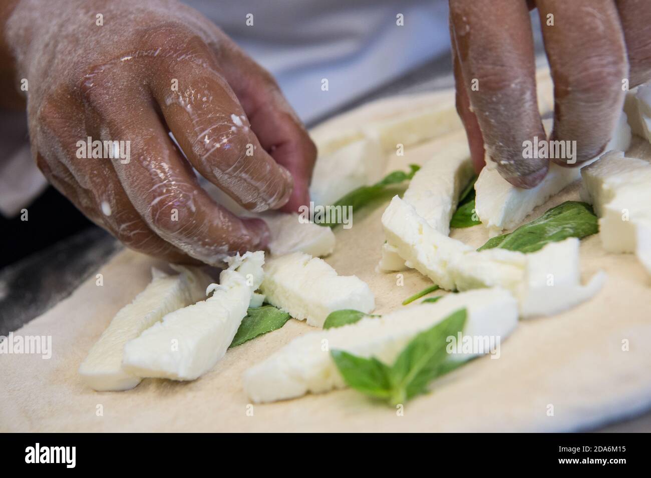 Dettaglio delle mani di uno chef pizzeria che lavora per le varie fasi di preparazione di una vera pizza italiana fatta in casa con farina di lievito e acqua. Foto Stock