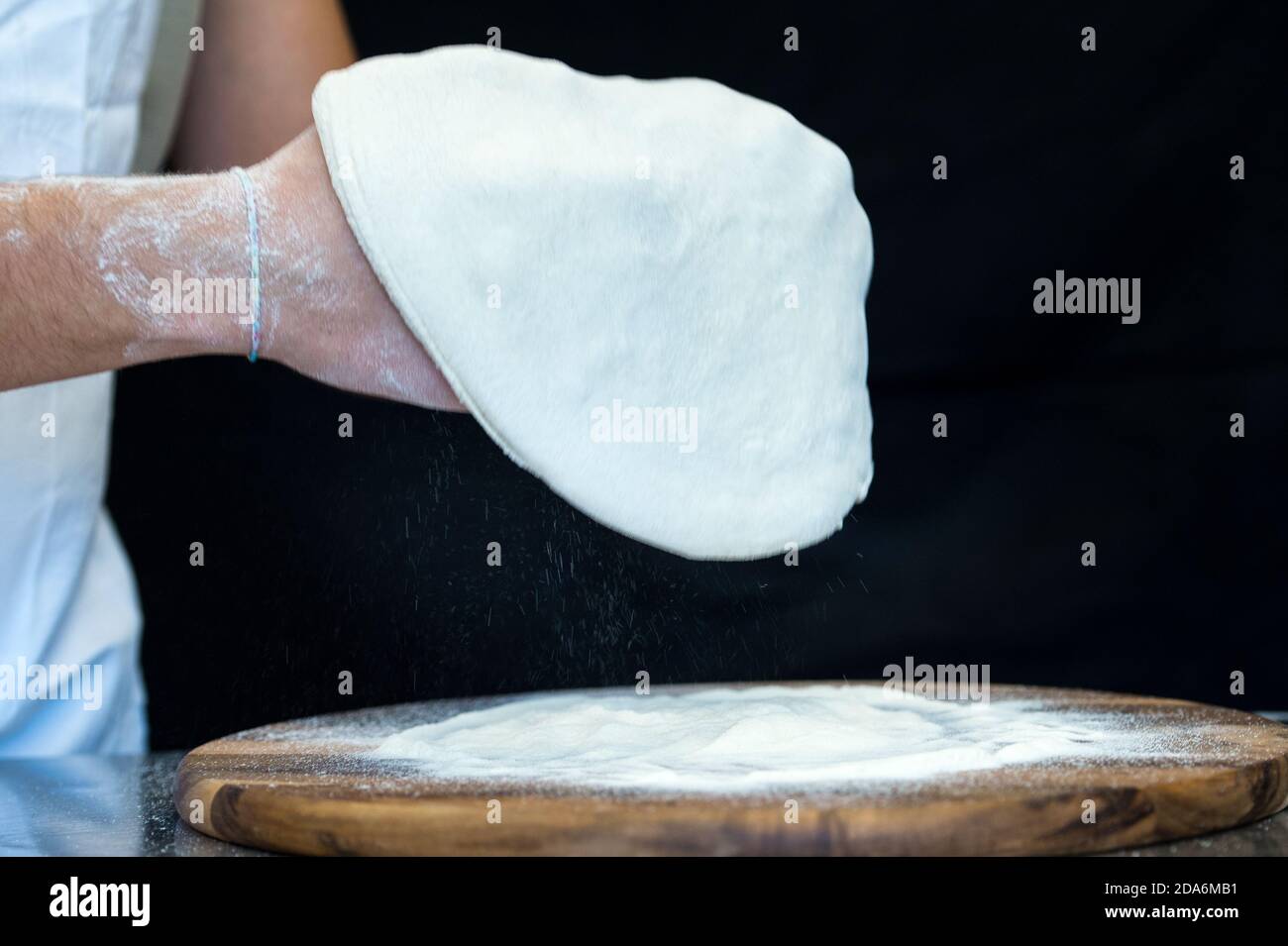 Dettaglio delle mani di uno chef pizzeria che lavora per le varie fasi di preparazione di una vera pizza italiana fatta in casa con farina di lievito e acqua. Foto Stock