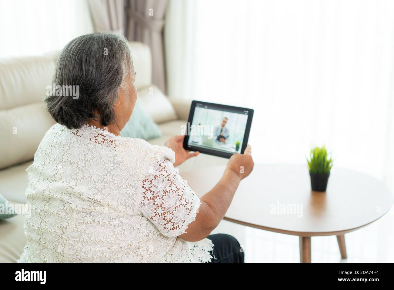 Vista posteriore della donna anziana che fa videochiamata con il suo medico con la sua sensazione di malessere su tablet digitale online assistenza sanitaria tecnologia digitale contro Foto Stock