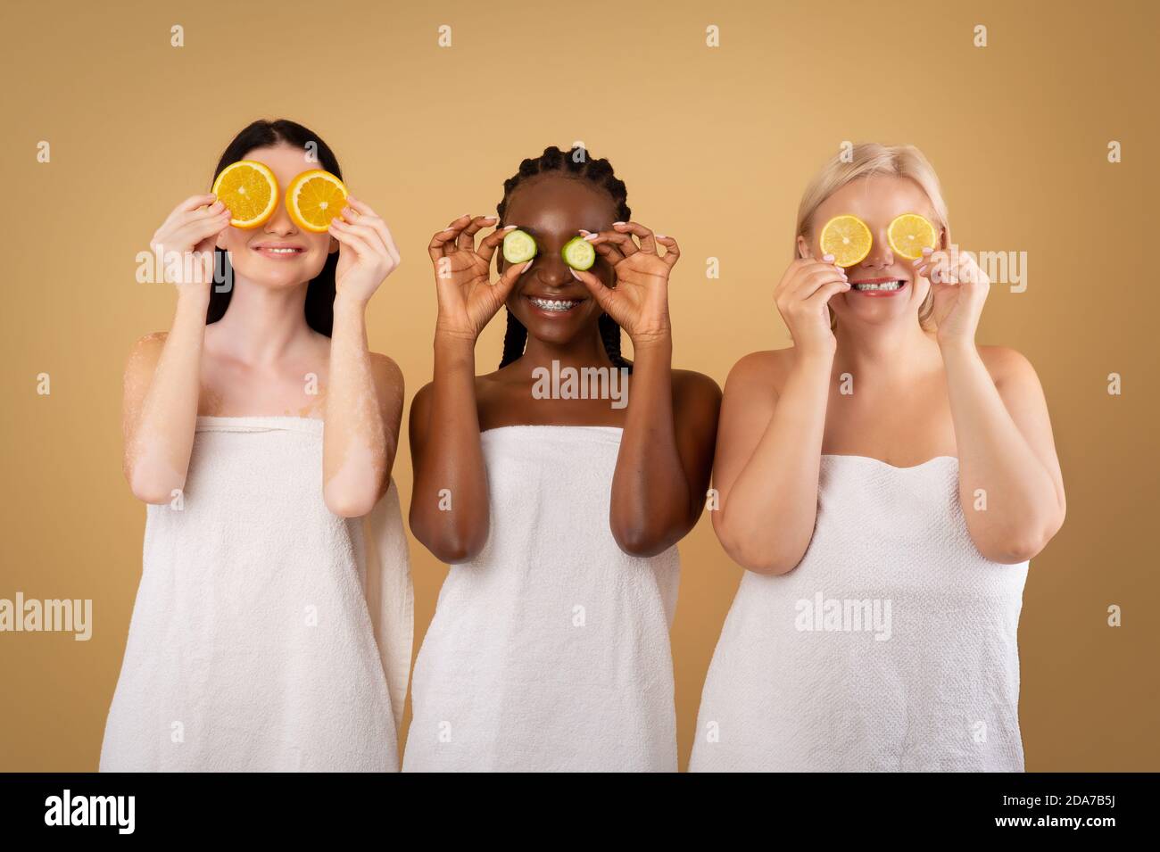 Corpo positivo Donne in Asciugamani coprendo gli occhi con cetriolo e. Fette arancioni Foto Stock