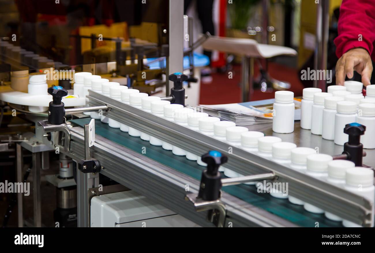 Bottiglia di plastica bianca su nastro trasportatore della macchina di riempimento delle capsule in linea di produzione. Industria farmaceutica Foto Stock