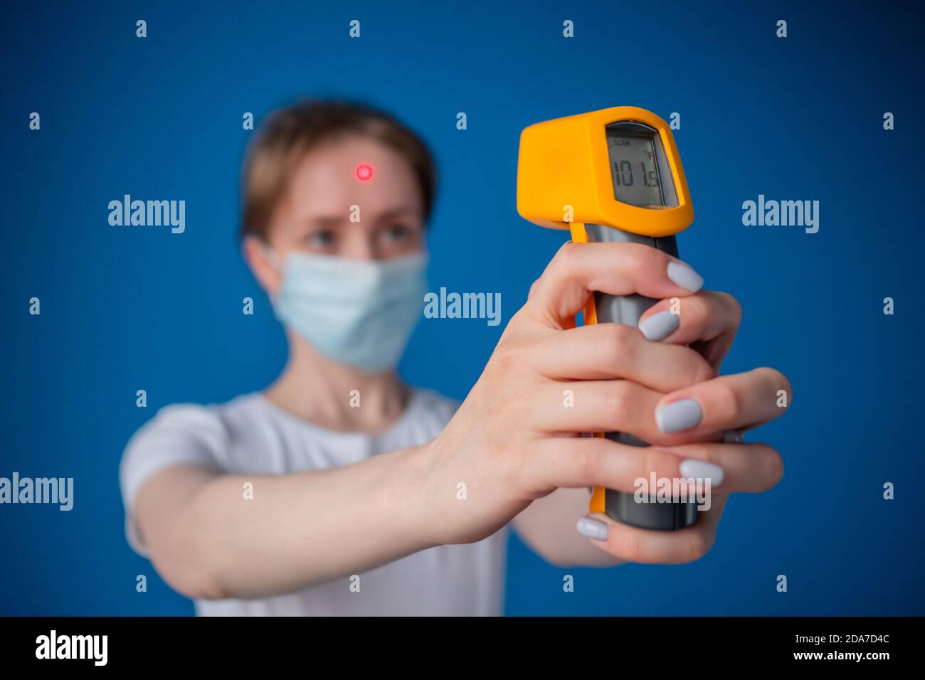 Donna in maschera medica con pirometro giallo per misurare la temperatura corporea - vista ravvicinata, messa a fuoco selettiva. Sanità, misurazione, malattia Foto Stock