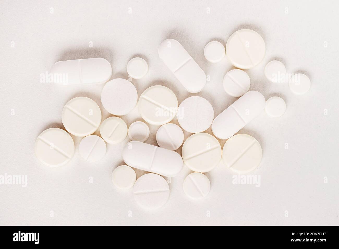 Le compresse e le capsule bianche di diverse misure si trovano su una superficie leggera, in primo piano, vista dall'alto. Medicinali e concetto di trattamento. Foto Stock