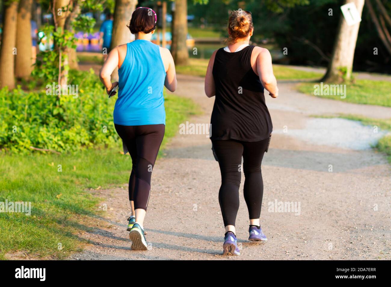 Vista posteriore di due donne che corrono fianco a fianco su un sentiero sterrato nei boschi al Belmont Lake state Park. Foto Stock