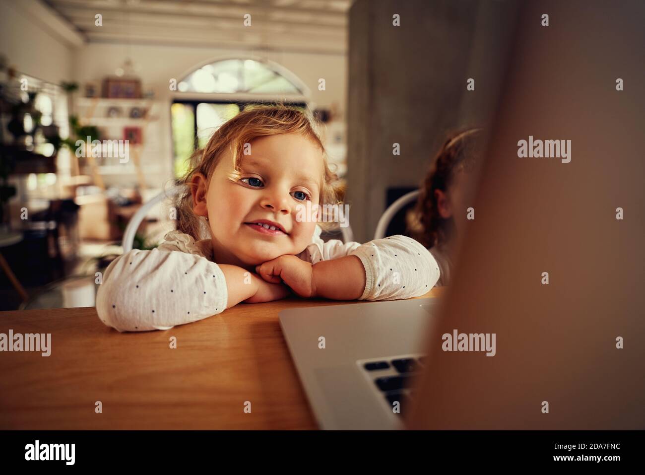 Ritratto di carina bambina guardando video sul computer portatile mentre appoggiandosi su un tavolo di legno a casa Foto Stock
