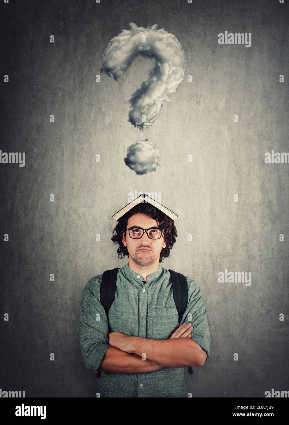 Perplesso studente ragazzo con il libro sulla sua testa, guardando stanco di apprendimento costante. Il giovane perplesso non preparato per gli esami, ha domande come interro Foto Stock