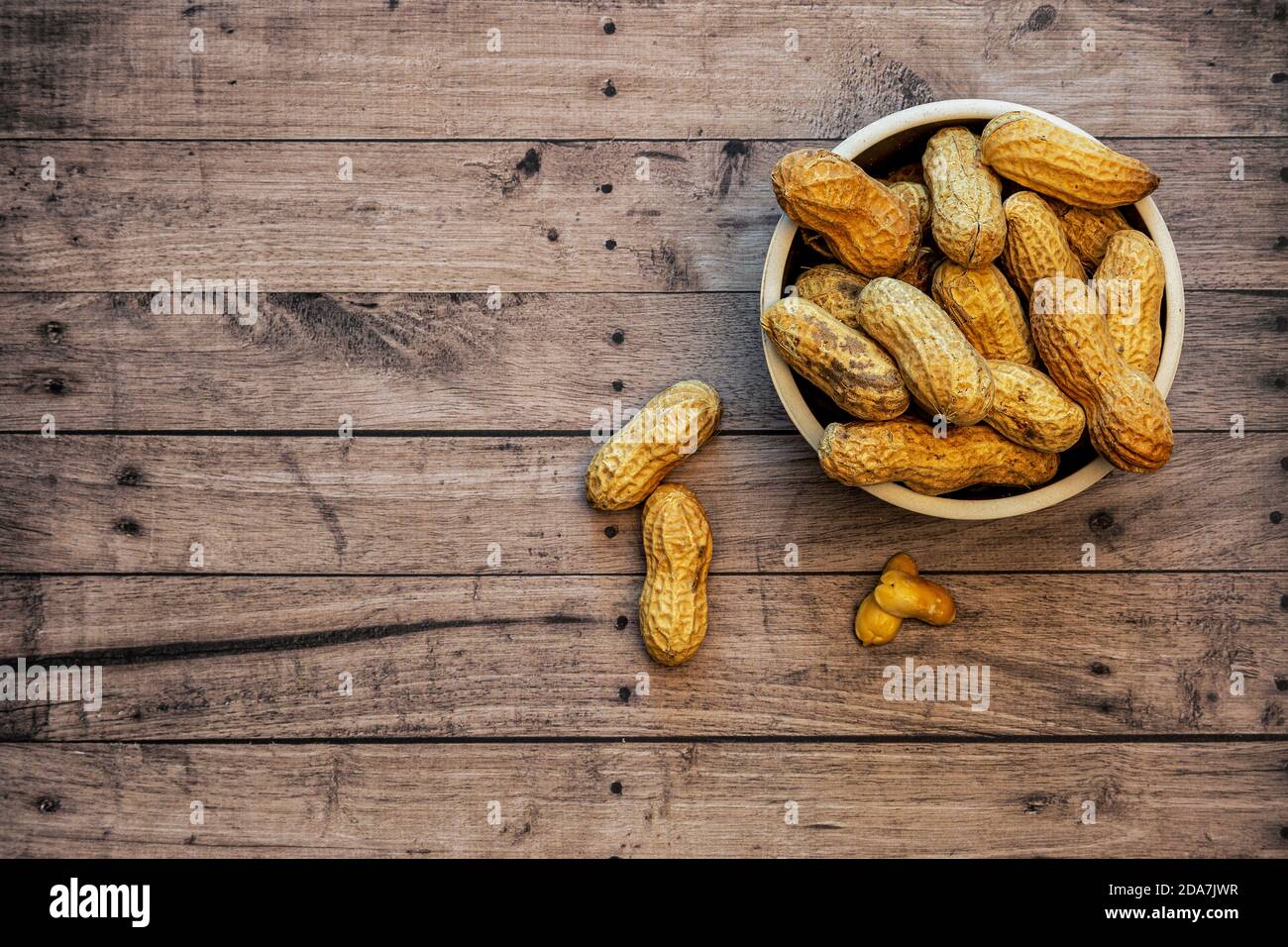 Ciotola di arachidi nelle conchiglie con sfondo in legno, spazio di copia e vista dall'alto Foto Stock