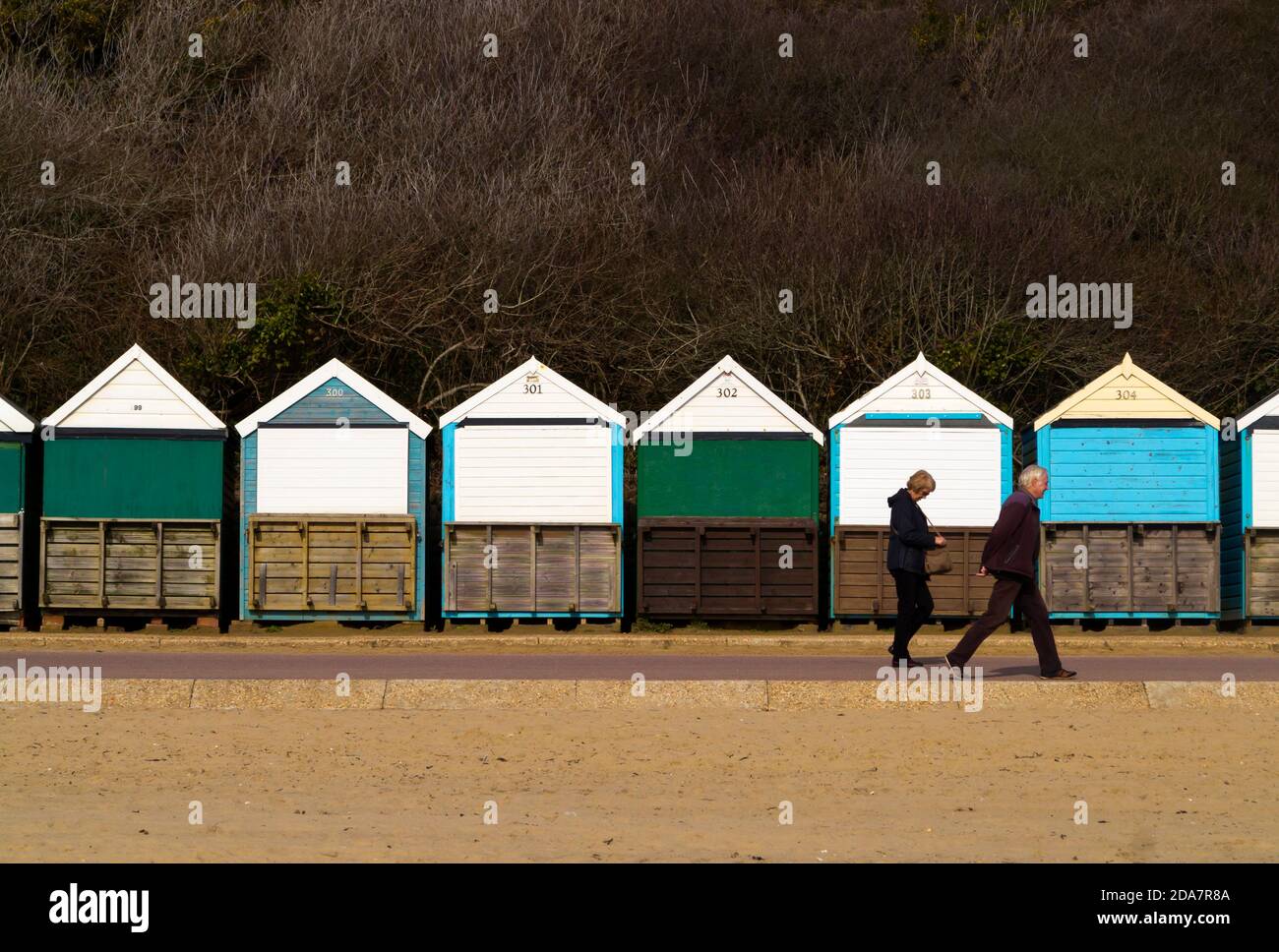 Coppie anziane che camminano davanti ai rifugi sulla spiaggia sul fronte mare Sulla spiaggia di Bournemouth, una località balneare sulla costa meridionale Dell'Inghilterra UK Foto Stock