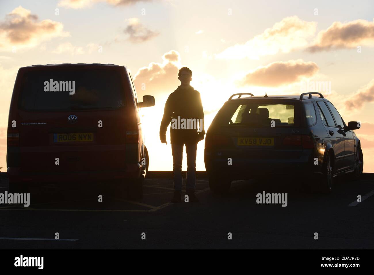 Qualcuno in piedi tra una macchina e un furgone, silhouette dal sole che tramonta alla fine di una bella giornata ad Aberaron Foto Stock
