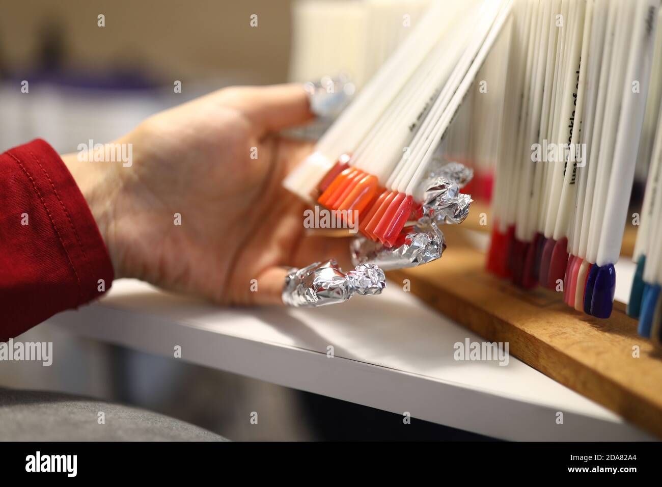 La mano femminile con lamina sui chiodi contiene campioni di tavolozza dei colori delle unghie. Foto Stock