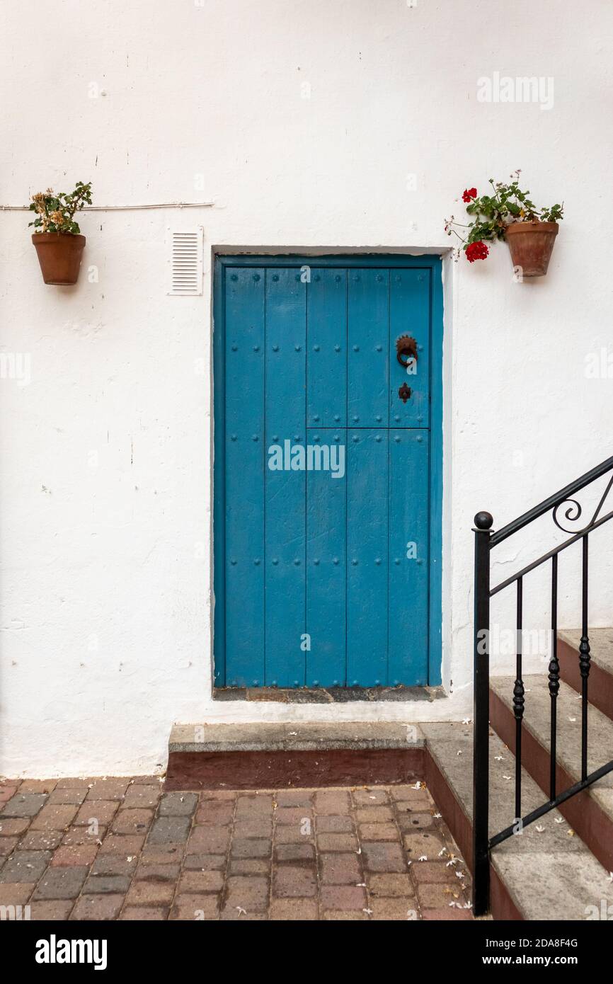 Porta di legno blu su una facciata bianca, tipica casa in un villaggio spagnolo tradizionale. Porta chiusa con manico in metallo, vasi di fiori con hangin gerani Foto Stock