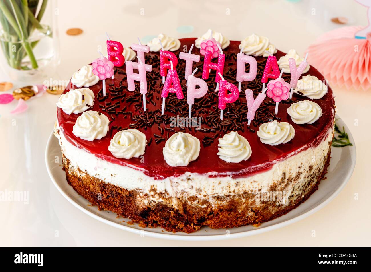 Torta di compleanno fatta in casa con candele di lettera con spruzzette di cioccolato e macchie di crema, sparato direttamente su un tavolo decorato in vetro bianco con confetti do Foto Stock