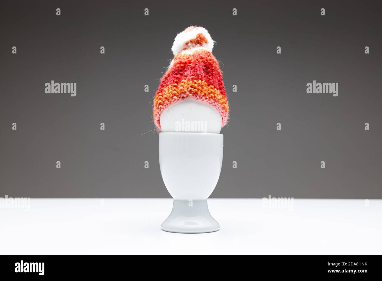 coppa d'uovo con uovo e un cappuccio di lana rosso arancione fatto in casa su sfondo grigio scuro su un tavolo bianco, spazio per la copia di testo o biglietti d'auguri per pasqua o chris Foto Stock