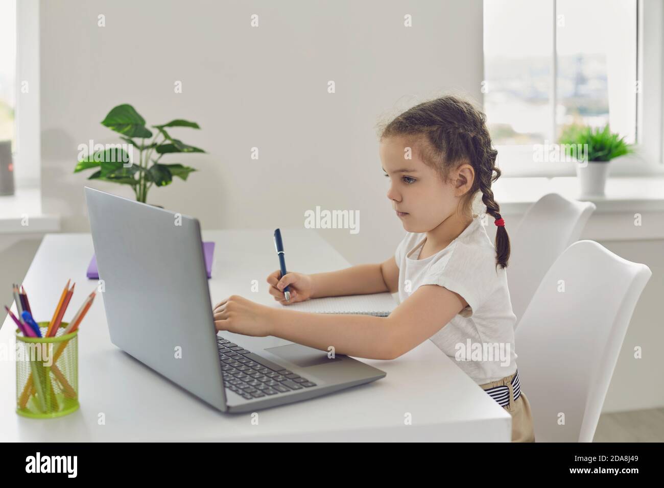Formazione online per bambini. Una ragazza con i pigtail sta guardando una video lezione usando un laptop in un salotto. Foto Stock