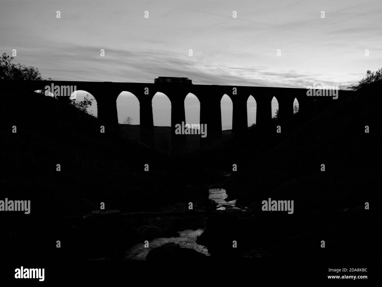 Locomotiva DRS classe 37 37407 che attraversa il viadotto Arten Gill, Dentdale sulla scenografica sistemazione per la linea ferroviaria di Carlisle che fa una silhouette al tramonto Foto Stock
