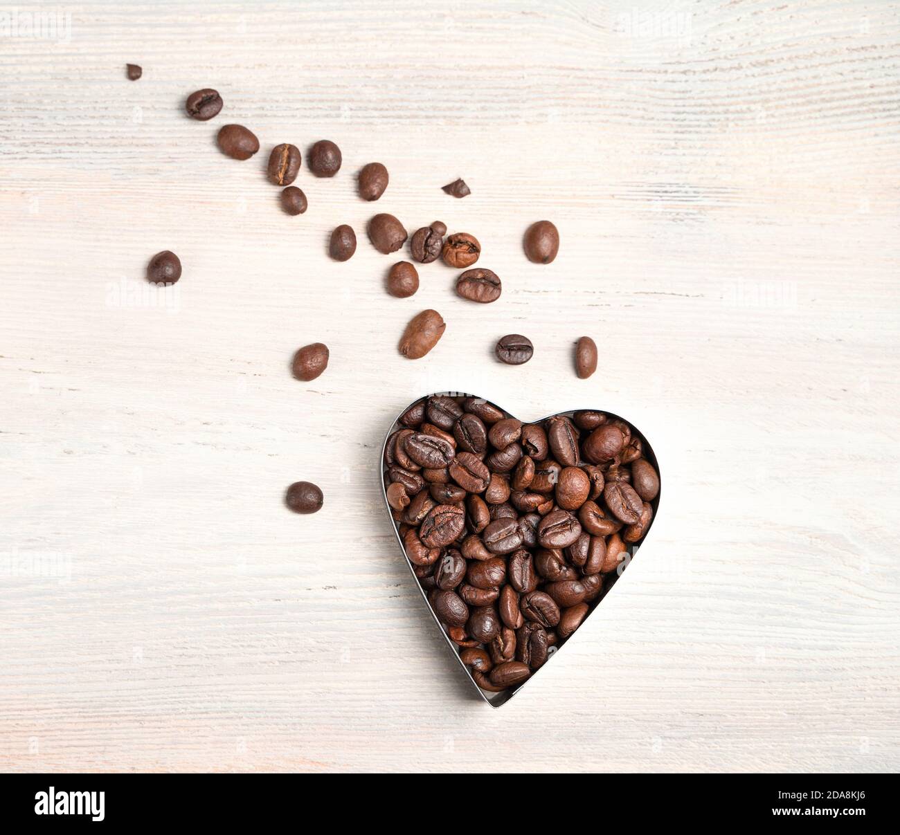 Chicchi di caffè a forma di cuore e grani sparsi nella forma della coda di una cometa su uno sfondo chiaro. Foto Stock