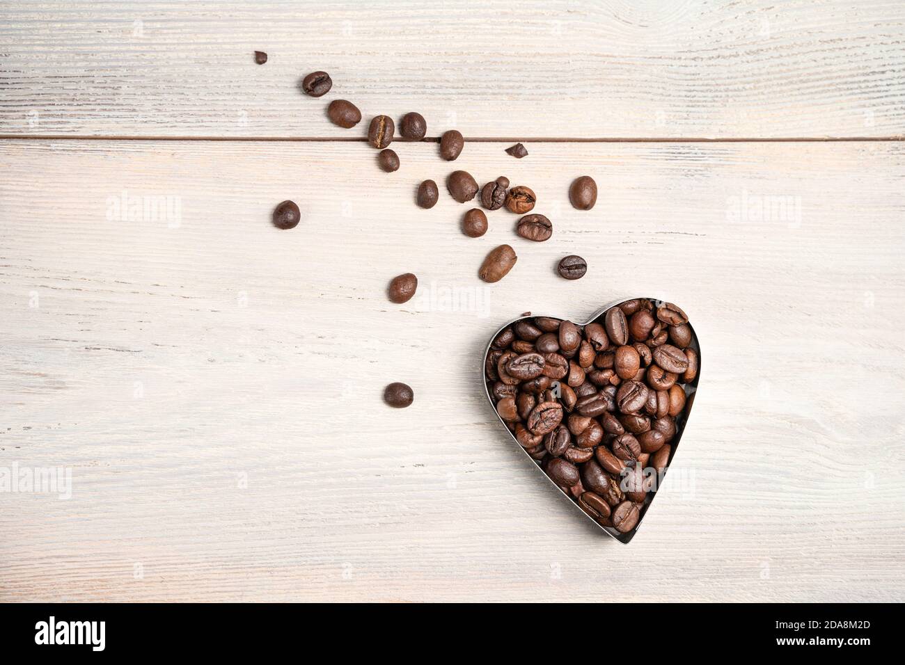 Cuore di caffè su sfondo chiaro. Un cuore volante con una coda di grani sparsi. Foto Stock