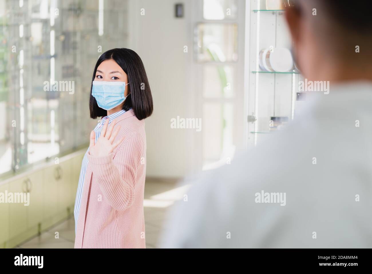 donna asiatica in maschera medica ondeggiando mano al farmacista dentro farmacia Foto Stock