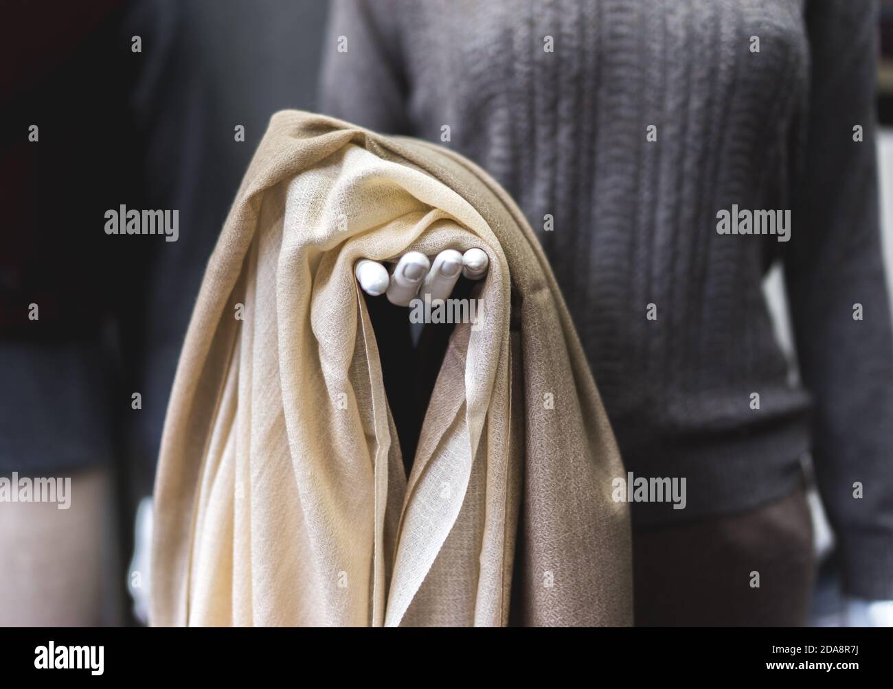 Titolo: Manichino con tessuto di cashmere beige chiaro in mano. Abbigliamento in pashmina naturale. Negozio di lana. Primo piano di una persona che tiene una sciarpa Foto Stock