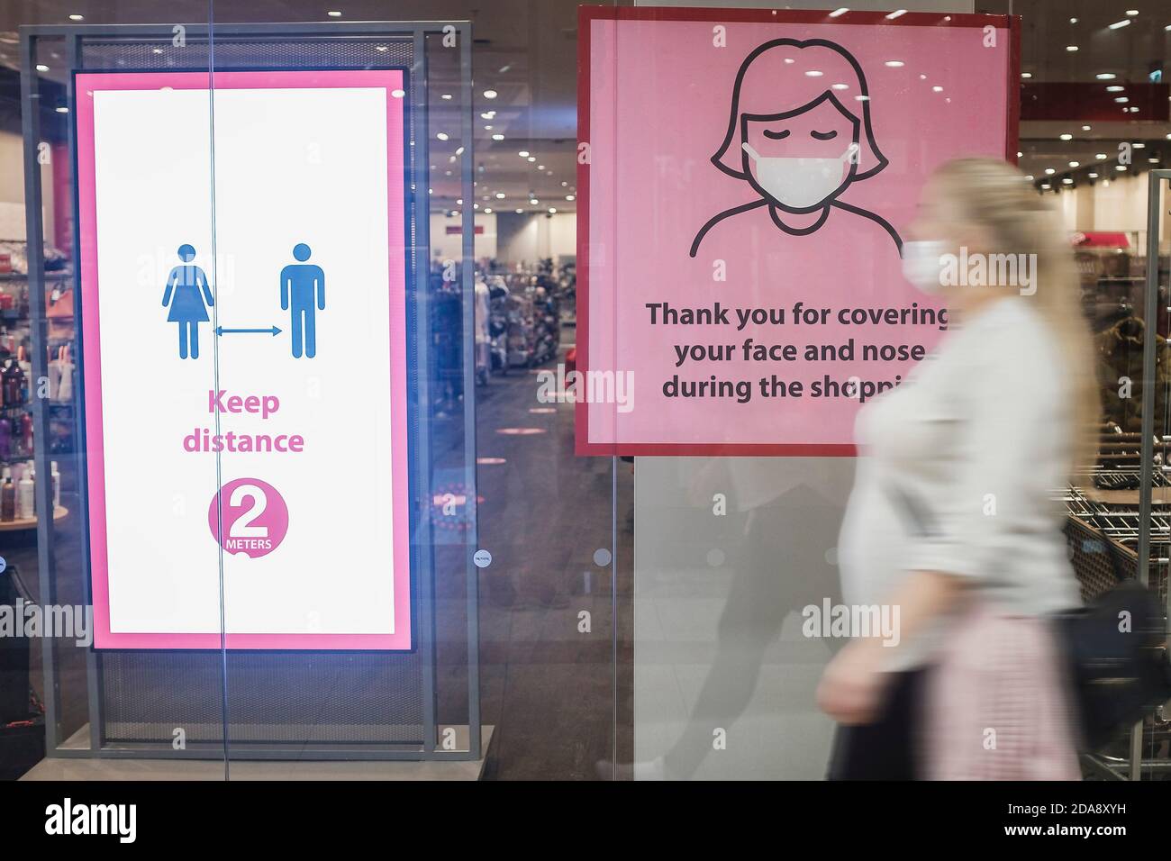 Istruzioni su shopping sicuro nella vetrina del centro commerciale durante la pandemia di Covid-19. Donna con maschera passa di fronte al negozio. Foto Stock
