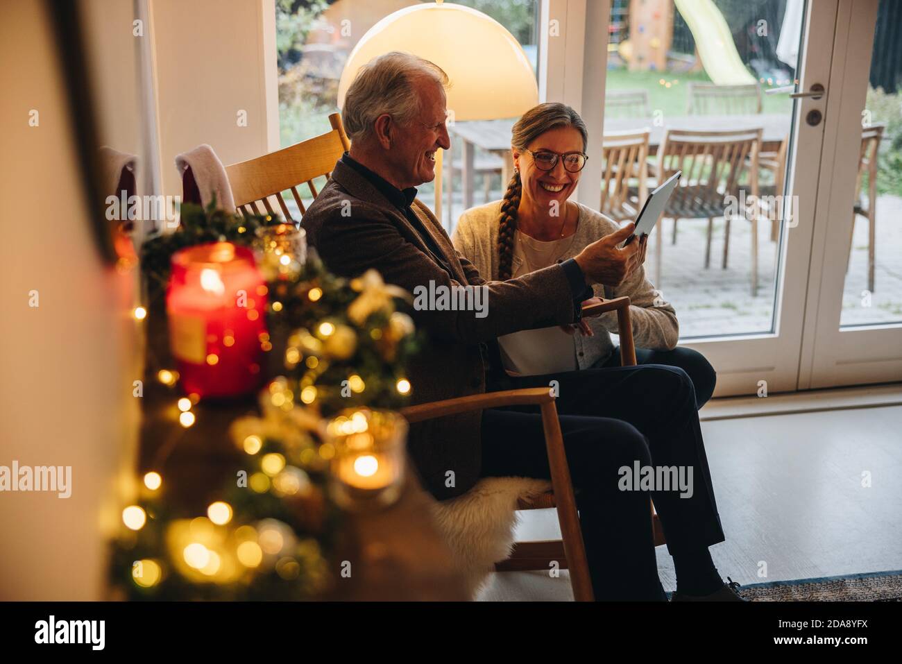 Coppia senior che utilizza un computer tablet per videochiamare la propria famiglia alla vigilia di Natale. Uomo anziano e donna che guardano al tablet digitale e sorridono durante Foto Stock