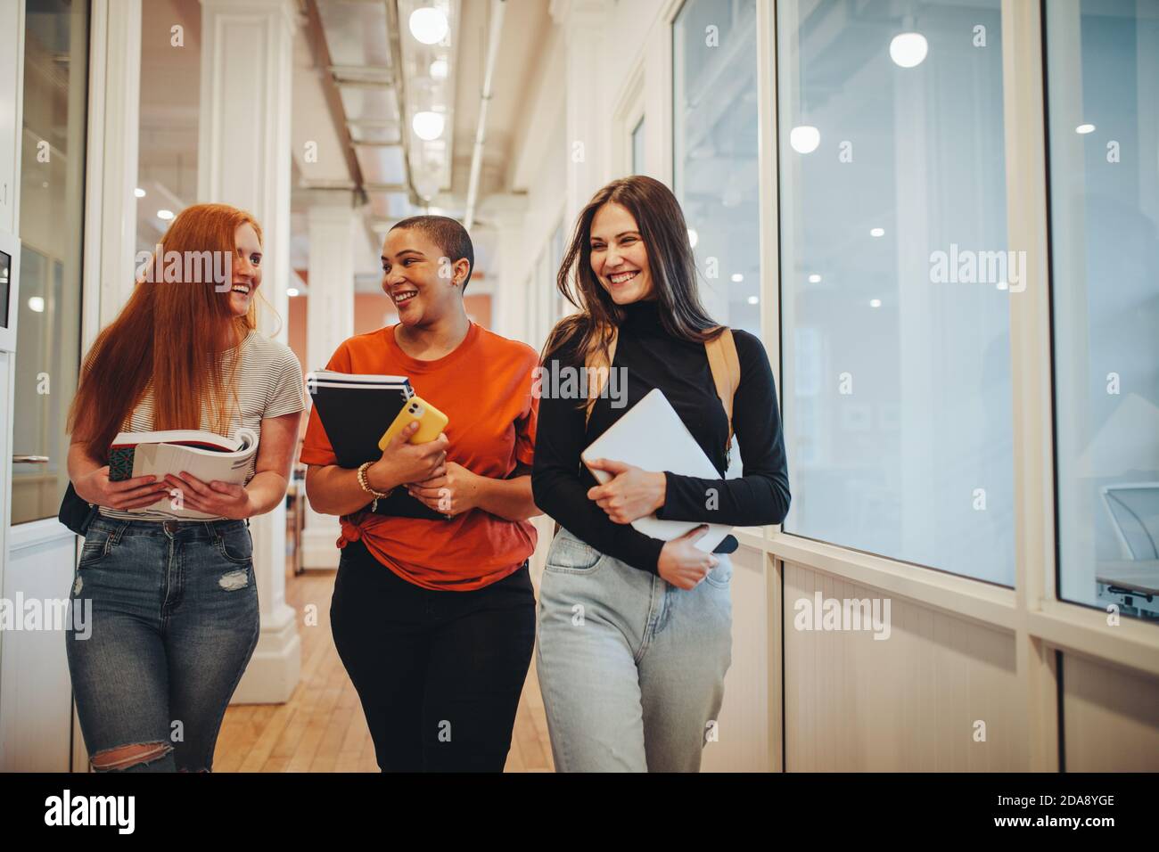 Ragazze sorridenti che camminano attraverso il corridoio della scuola superiore dopo la loro classe. Tre studenti universitari femminili dopo la lezione. Foto Stock