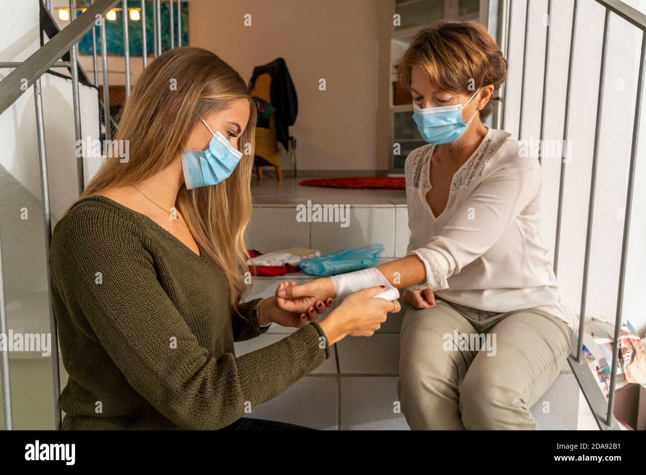 Misure di pronto soccorso in condizioni di corona, applicazione di una fasciatura, dopo un incidente in casa, con una maschera per naso e bocca, al momento del primo soccorso Foto Stock