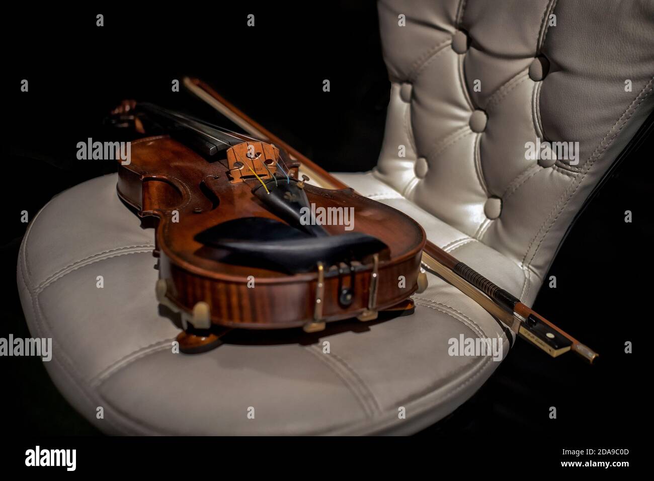 Ancora vita strumento musicale. Violino e arco su una sedia in pelle bianca Foto Stock