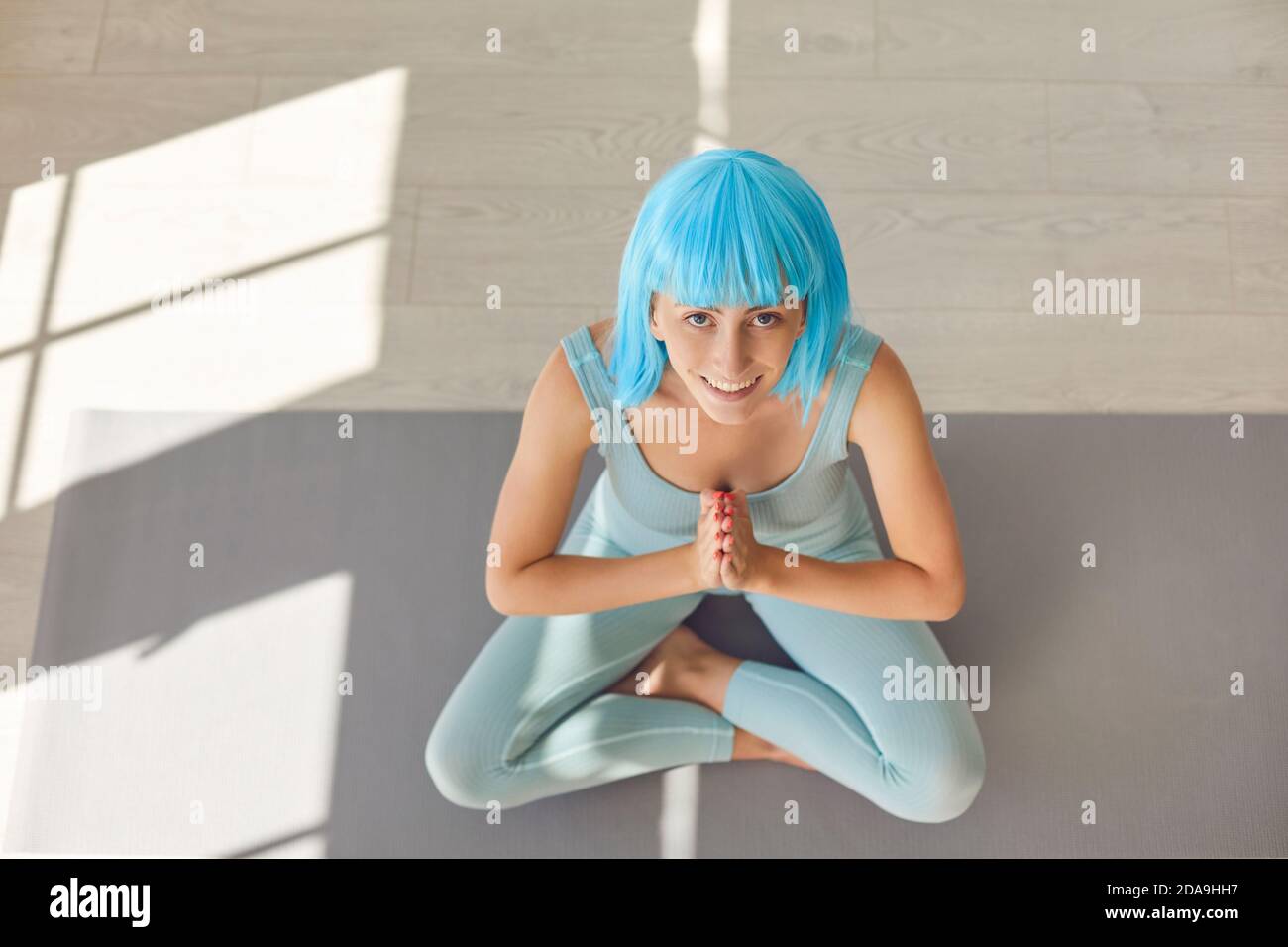 Giovane donna seduta a croce con le mani sul tappeto yoga Si è Unito a Namaste guardando la fotocamera Foto Stock