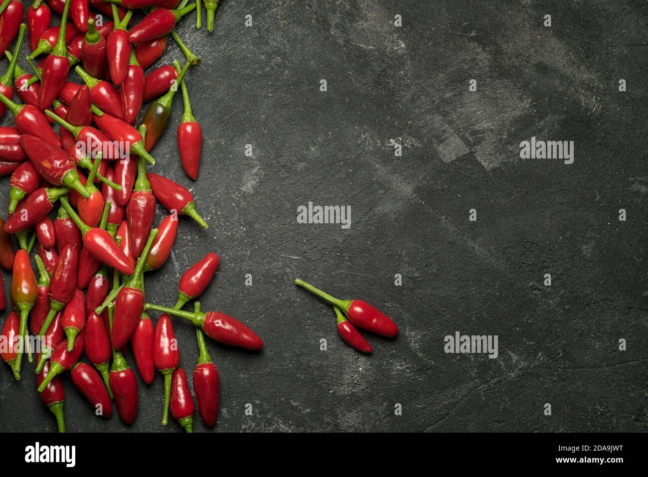 Peperoncini rossi caldi a lato, cornice su un tavolo nero, vista dall'alto con spazio per la copia del testo culinario. Foto Stock