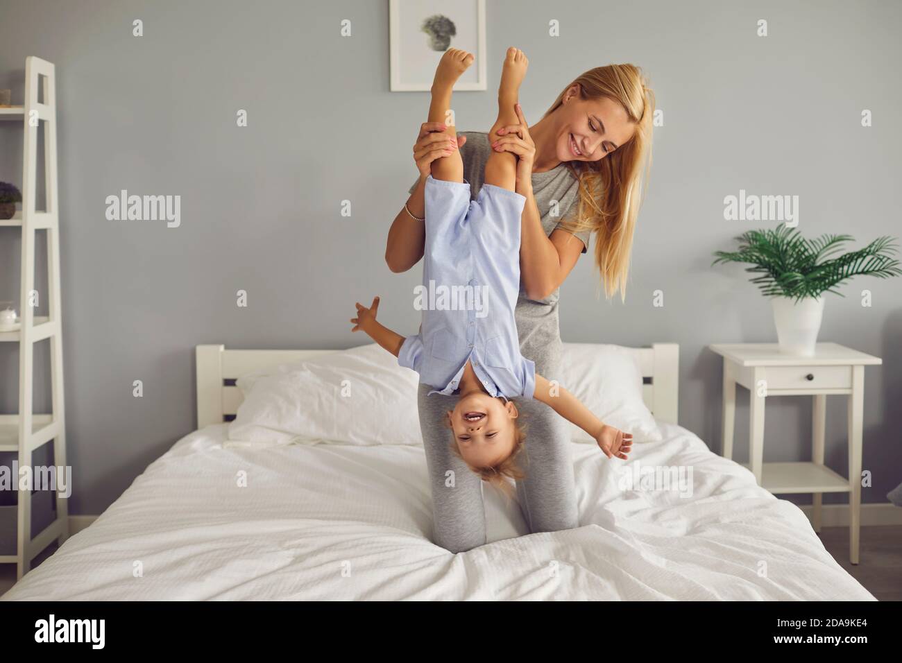 Felice giovane mummia godendo il fine settimana a casa e giocando con il suo divertente figlio del bambino su un comodo letto Foto Stock