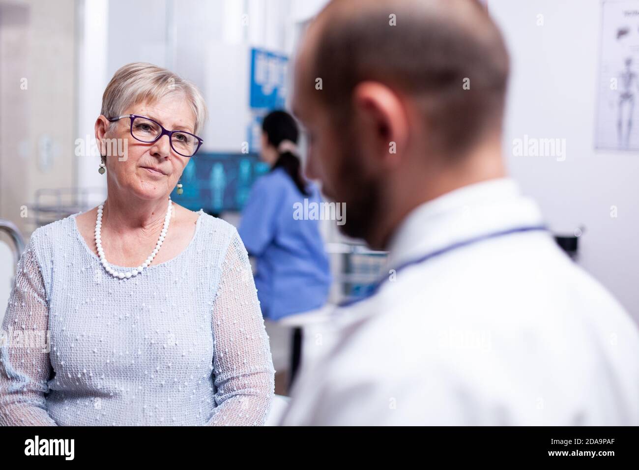 Donna che ascolta medico durante l'esame in sala di consultazione clinica. Convertation con la medicina medica clinica di roba, anziani, cappotto, appunti. Foto Stock