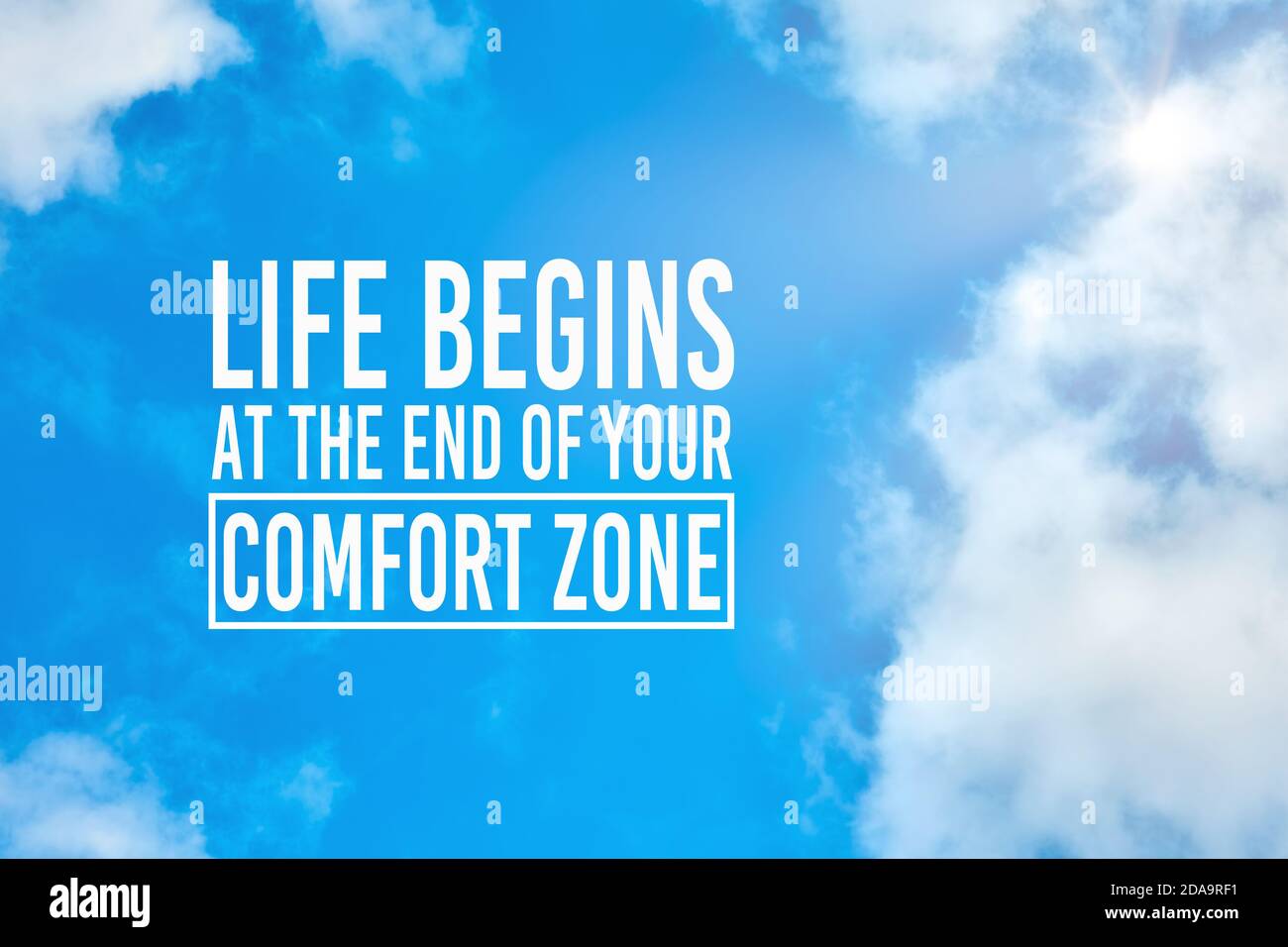 La vita inizia alla fine della tua zona di comfort citazione ispiratrice contro il cielo blu con le nuvole di sfondo. Fare un cambiamento, evolversi o migliorare personale Foto Stock