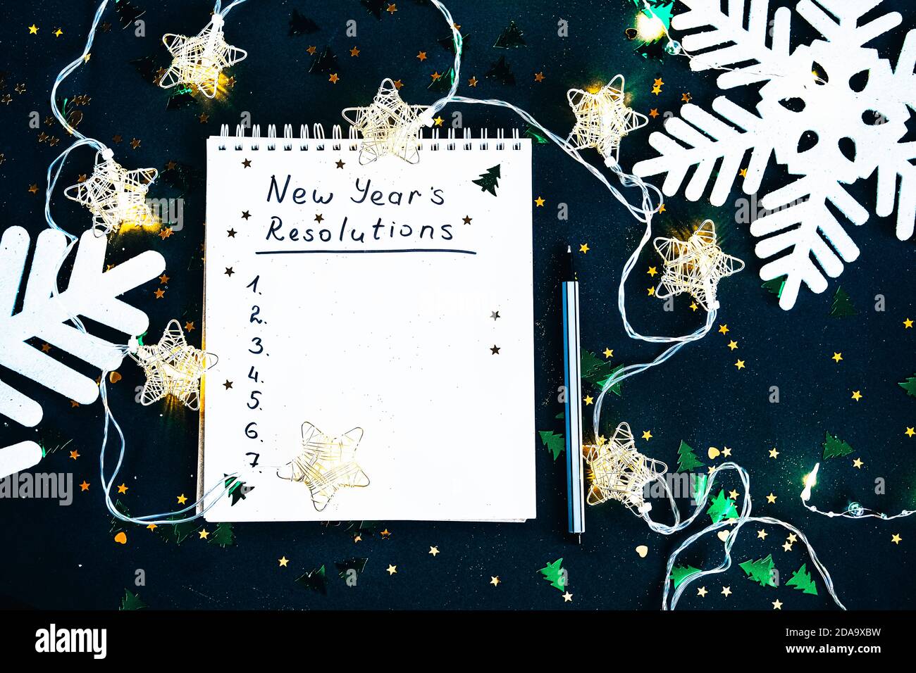 Gli obiettivi del nuovo anno. L'elenco delle risoluzioni in un blocco note su sfondo verde scuro. Concetto di motivazione delle aspirazioni di risoluzione Foto Stock