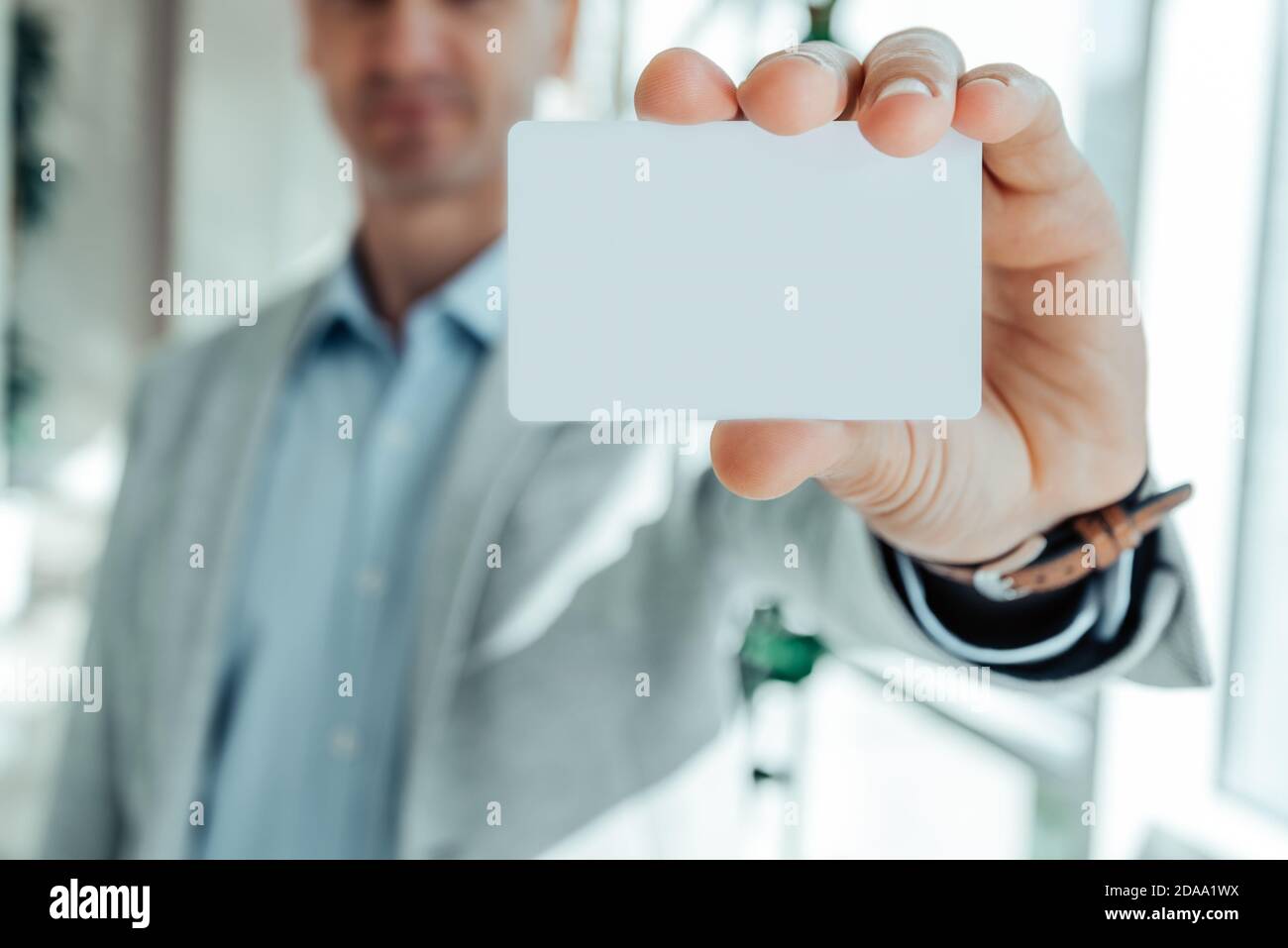 un uomo in una giacca grigia e una camicia blu che tiene un biglietto da visita spinto in avanti. mockup. Foto Stock