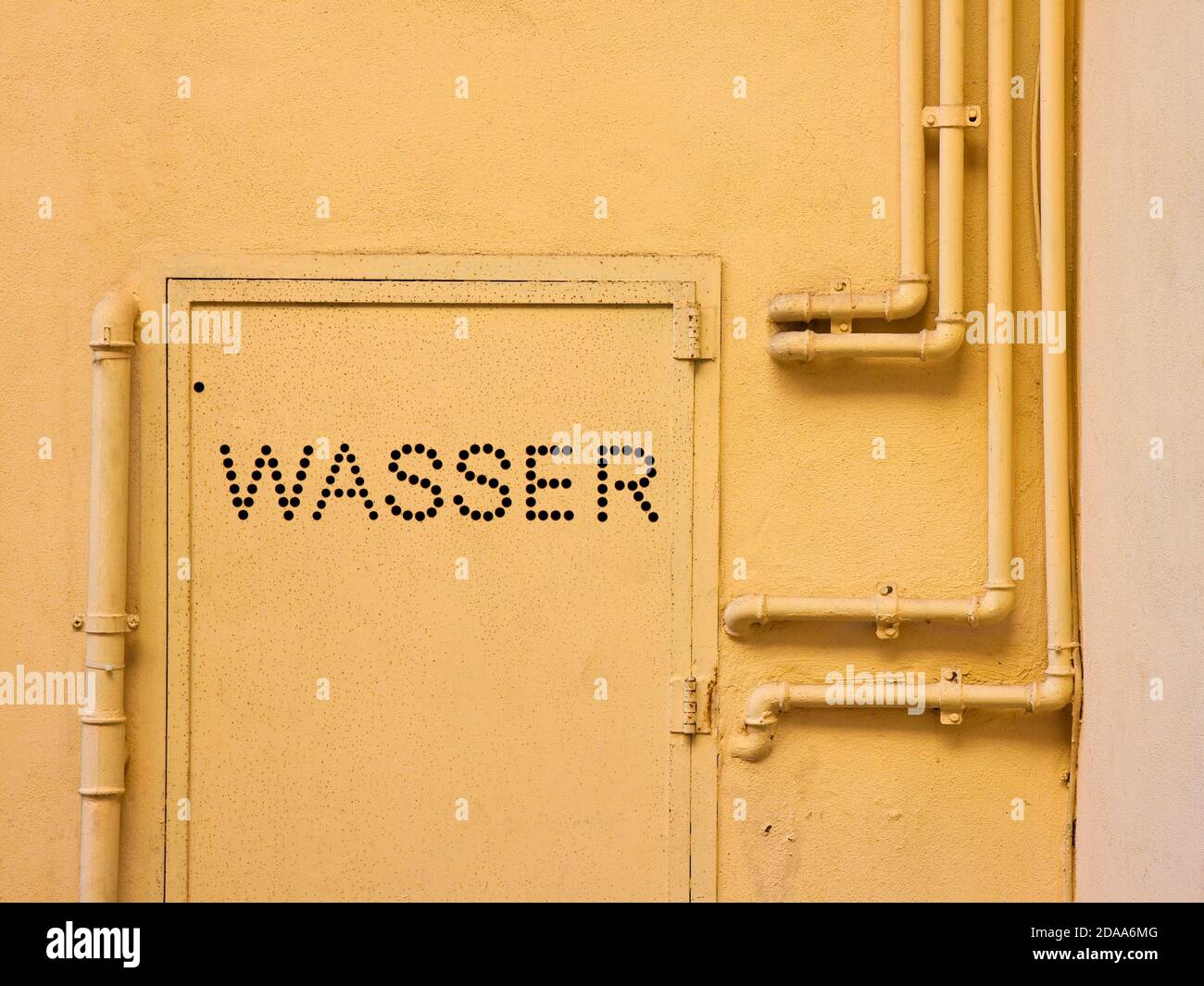 Vecchi tubi in metallo d'acqua fissati con staffe davanti a. una parete in gesso con scatola in metallo per misuratore di acqua - Scritto in tedesco Foto Stock