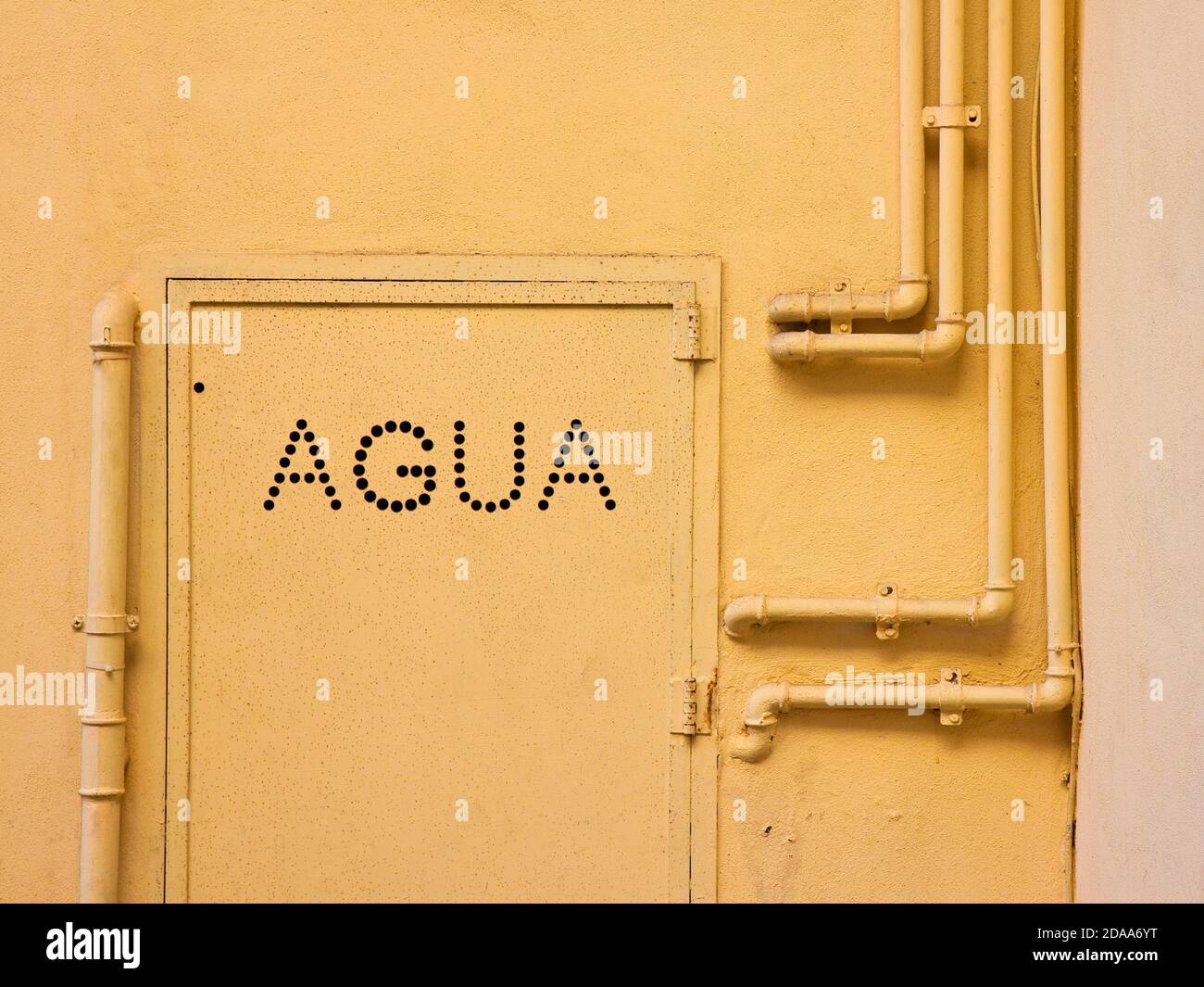 Vecchi tubi in metallo d'acqua fissati con staffe davanti a. una parete in gesso con scatola in metallo per misuratore di acqua - Scritto in spagnolo Foto Stock