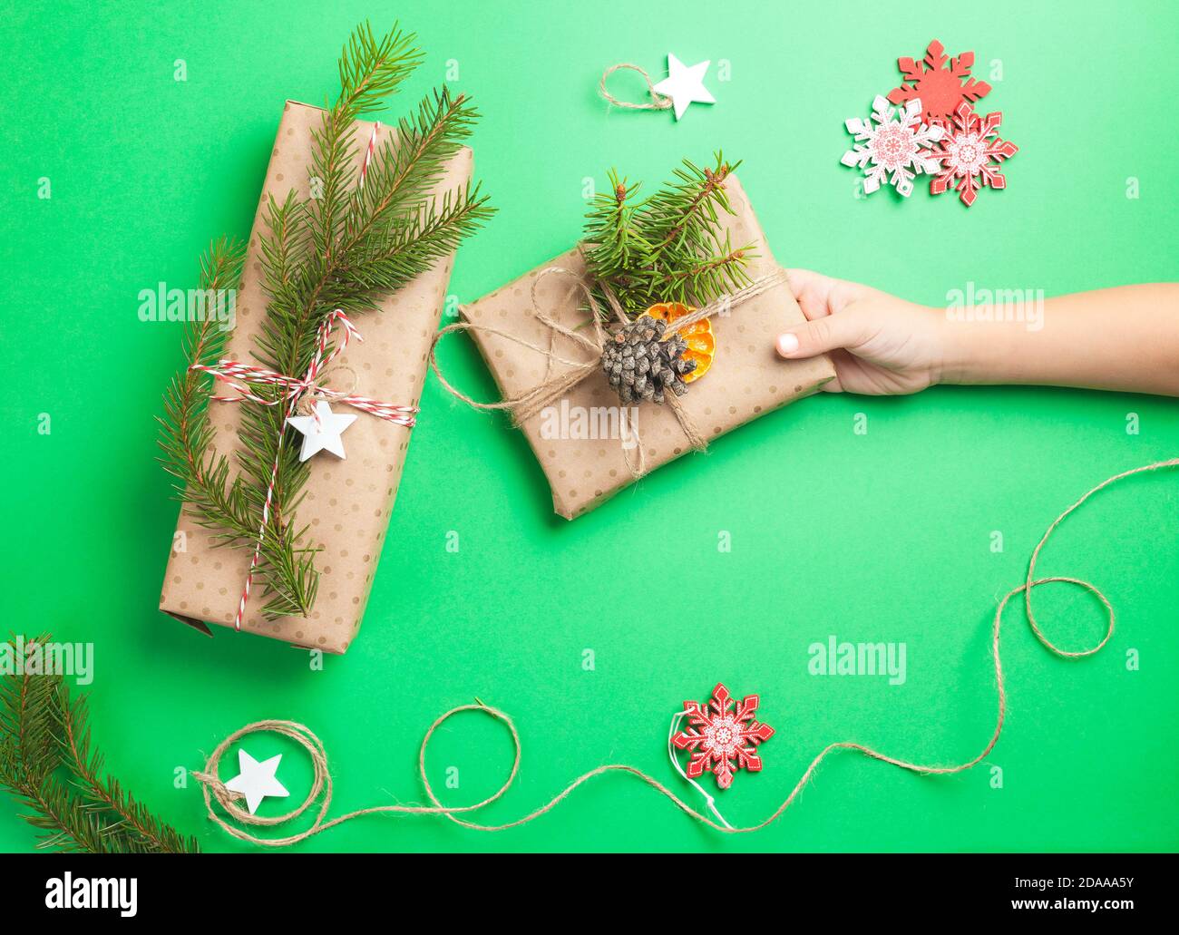 Zero rifiuti scatole regali di Natale avvolte in carta artigianale su sfondo verde . La mano del bambino ne tiene uno presente Foto Stock