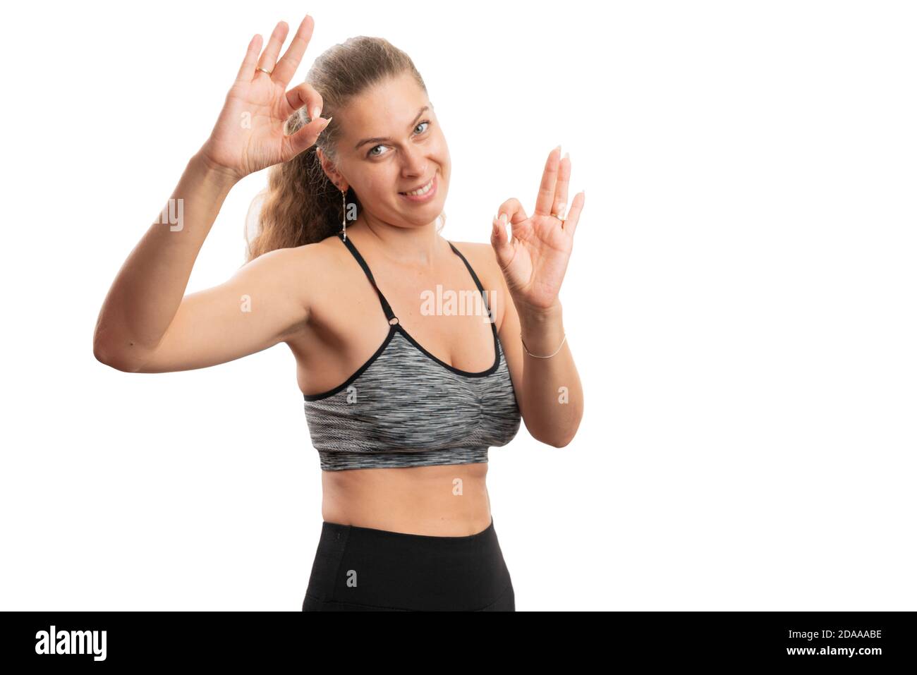 Modello femmina sorridente che mostra un doppio gesto corretto con le dita abbigliamento sportivo con spazio vuoto per la pubblicità isolato su bianco sfondo Foto Stock
